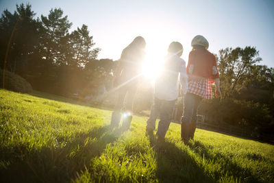 Full length of friends walking on grassy field during sunny day