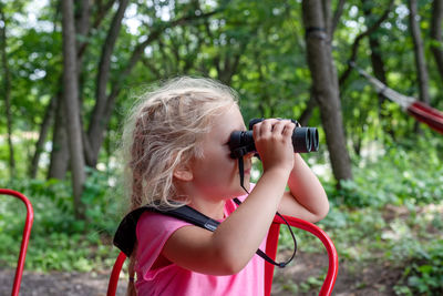 Girl holding plant against trees