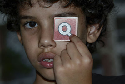 Close up portrait of boy holding letter q in front of eye