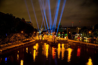 Illuminated city by river against sky at night