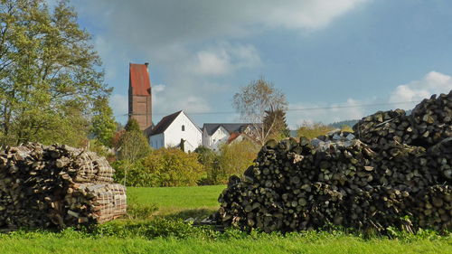 Stack of logs on field by buildings against sky