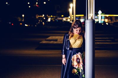 Woman standing on illuminated street at night