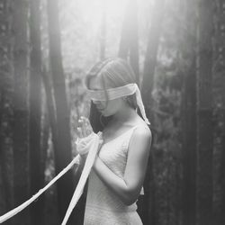 Blindfolded woman with wrapped hands standing against trees at forest