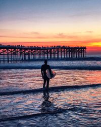 Silhouette woman standing on beach against sky during sunset