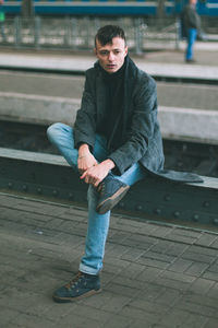 Portrait of young man sitting on footpath