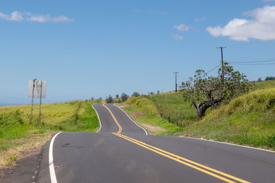 Country road amidst field against sky