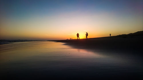 Silhouette people on beach against sky during sunset