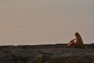 Woman sitting on rock at sunset
