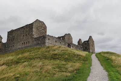 Stone wall against sky with path leading to ruins