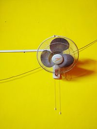 Low angle view of electric fan mounted on yellow wall at home