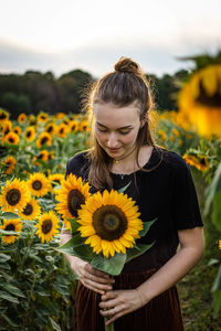 Portrait of young woman with sunflower standing on field