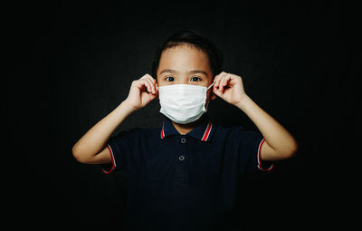 Portrait of boy holding camera over black background