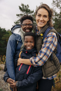 Portrait of father and mother embracing son while standing in forest