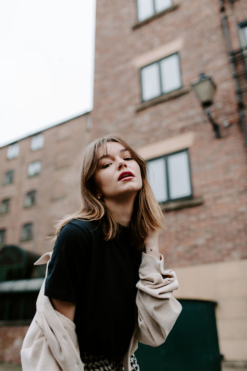 architecture, one person, building exterior, built structure, young women, real people, lifestyles, young adult, front view, standing, women, focus on foreground, leisure activity, day, waist up, hairstyle, hair, casual clothing, beautiful woman, outdoors, contemplation