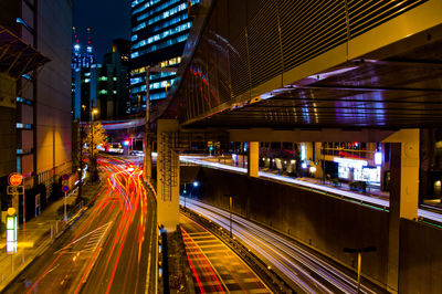 Light trails on road amidst illuminated buildings at night