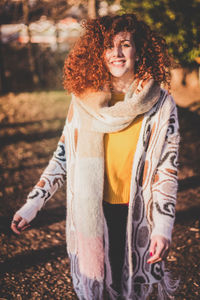 Portrait of smiling young woman standing against trees during sunny day