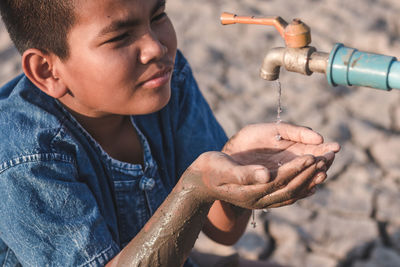 High angle view of boy with hands cupped gesturing by faucet during summer