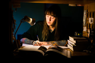 Young woman writing in book sitting at home