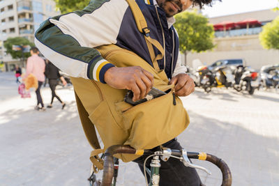 Casual businessman with bicycle taking cell phone out of backpack in the city, barcelona, spain