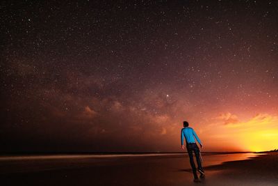 Rear view of man standing at beach against star field