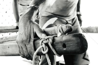 Midsection of man holding wood and rope