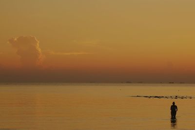 Woman standing in sea against orange sky during sunset