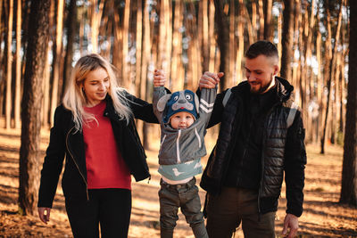 Happy young mother and father holding their child by hands in forest