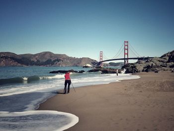 Photographer photographing golden gate bridge against clear blue sky