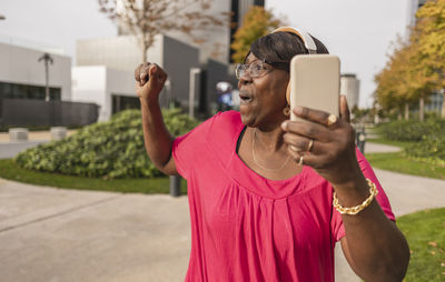 Happy woman holding smart phone enjoying at park