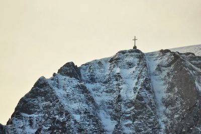 Low angle view of cross snowcapped mountain peak against clear sky