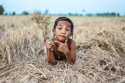 Portrait of boy sitting on field against sky