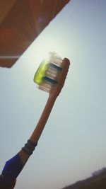 Low angle view of man holding drink against sky