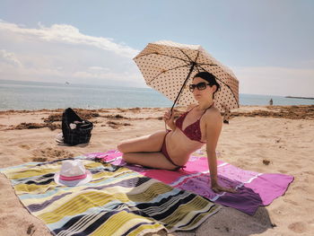 Young woman with umbrella on sand at beach against sky