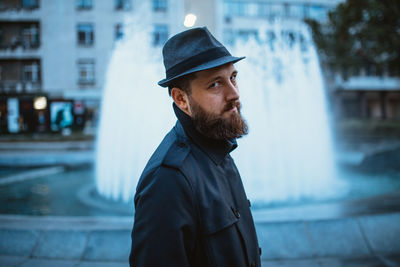 Portrait of man standing against fountain in city