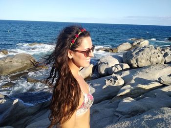 Beautiful young woman on rock at beach against sky