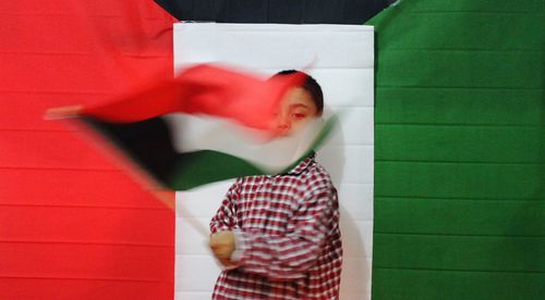 Portrait of boy waving flag against wall