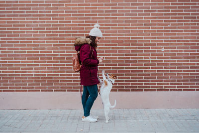 Woman with dog standing on footpath against wall