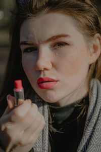 Girl holding a bottle of red lipstick, apply lipstick on her lips, with freckles on her face 