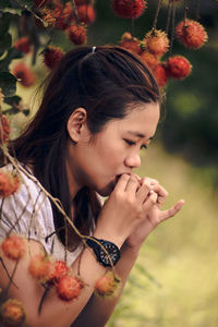 Side view of young woman holding red flowering plant