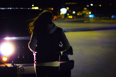 Rear view of woman standing by sports utility vehicle on street during night