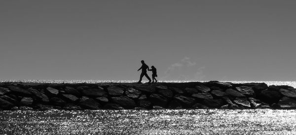 Silhouette father and son walking on groyne amidst sea against sky