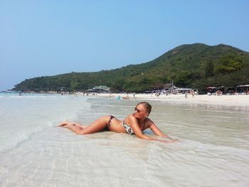 Woman in bikini lying at beach against clear sky