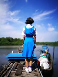 Rear view full length of girl wearing uniform standing on boat against sky