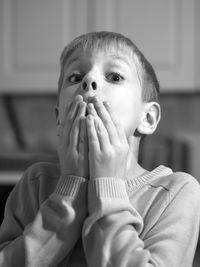 Close-up portrait of shocked boy covering mouth at home