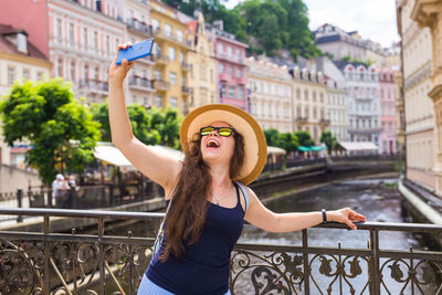 Cheerful woman doing selfie while standing on bridge