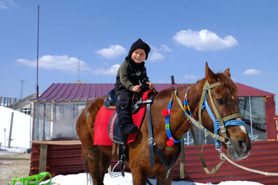 Rear view of child riding horse against sky