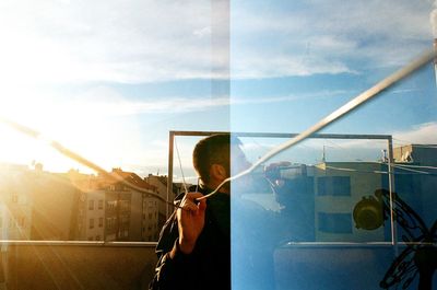 Man skateboarding on glass window against sky