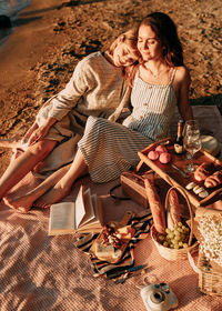 Happy woman friends relaxing on the beach with picnic on a sunny day