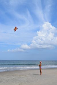 Woman flying over beach against sky