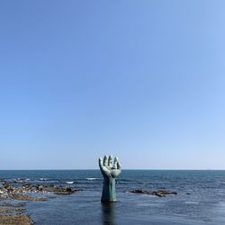 Statue by sea against clear blue sky